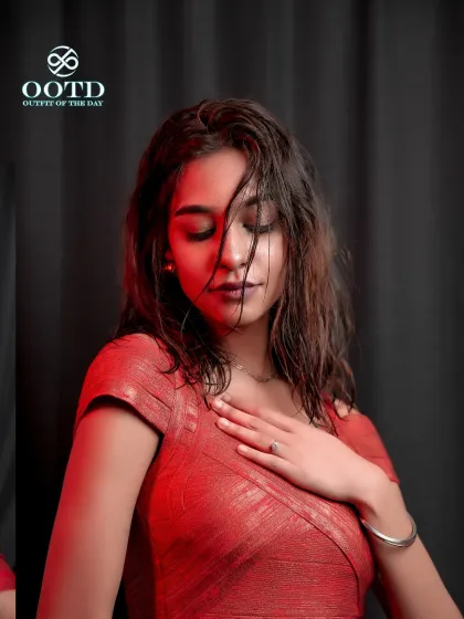 A close-up portrait with dramatic red lighting, highlighting the texture of the dress and the model's serene yet powerful expression.