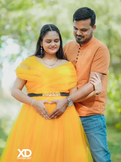 A loving couple's portrait in a garden, with their hands joined to form a heart on the baby bump.