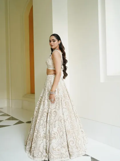 A full-length shot of a magnificent white chikankari-style lehenga. The styling is kept elegant and modern with a statement diamond necklace and long, flowing hair.
