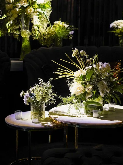 A close-up of a table centerpiece at a modern cocktail party, with white florals in a glass vase, surrounded by candles.