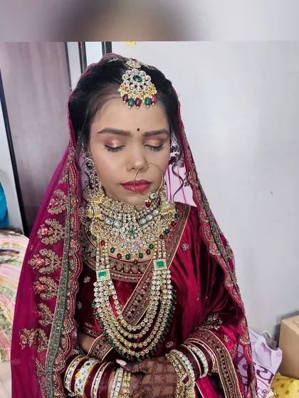 A beautiful bride in a velvet maroon lehenga. The makeup features a soft smokey eye and a bold lip, creating a look of timeless elegance.