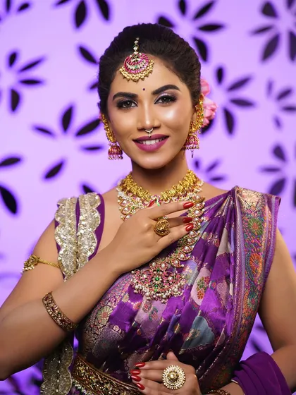A close-up of a flawless HD bridal makeup look. Notice the smooth skin finish, the perfectly blended cut-crease eyeshadow, and how the makeup harmonizes with the bride's purple silk saree and temple jewellery.