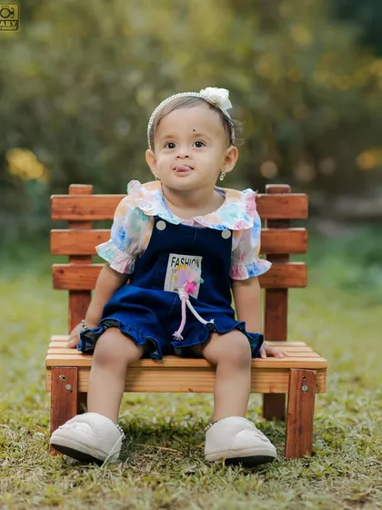 A cute portrait of a little girl sitting on a bench in the park, with a sweet, curious expression.