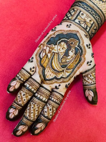 A stunning Radha Krishna portrait nestled in the palm of a bridal mehendi. The use of dark, bold lines makes the divine couple the centerpiece of the design.
