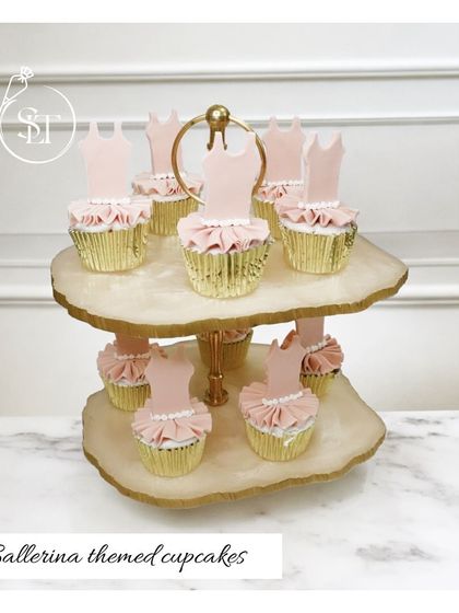 Adorable ballerina-themed cupcakes, perfect for a little dancer's party. Each cupcake is topped with a pink frosting tutu and a ballerina dress silhouette, presented on a beautiful two-tiered stand.