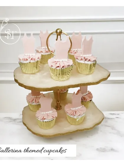 Adorable ballerina-themed cupcakes, perfect for a little dancer's party. Each cupcake is topped with a pink frosting tutu and a ballerina dress silhouette, presented on a beautiful two-tiered stand.