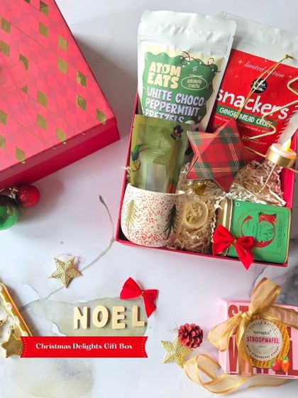 The Christmas Delights Gift Box is all about festive charm. This image showcases the Noel-themed treats, including gingerbread snackers and a Christmas-tree-patterned mug.