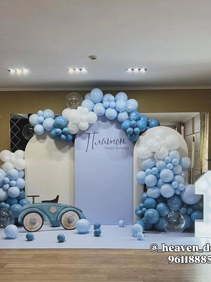 A stylish and modern car-themed first birthday in soft blue and white. The setup includes a vintage car prop, a large light-up number '1', and a beautiful balloon cloud arrangement over arched backdrops.