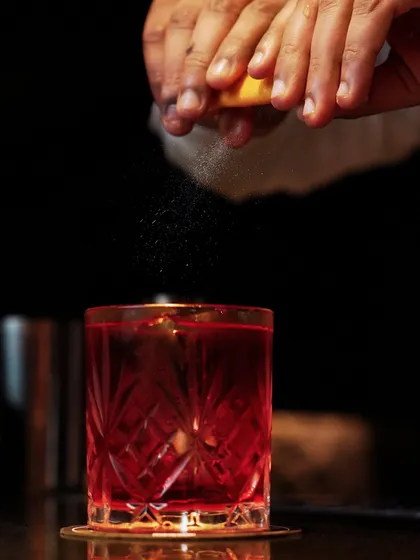 A whisper of citrus or a twist of smoke, every cocktail story starts at the rim. This action shot shows the moment a lemon peel is expressed over a drink, releasing essential oils.