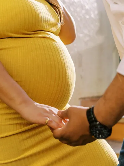 A close-up on the details: their joined hands over her belly. The vibrant yellow of her dress and the texture of the fabric add visual interest to this intimate shot.