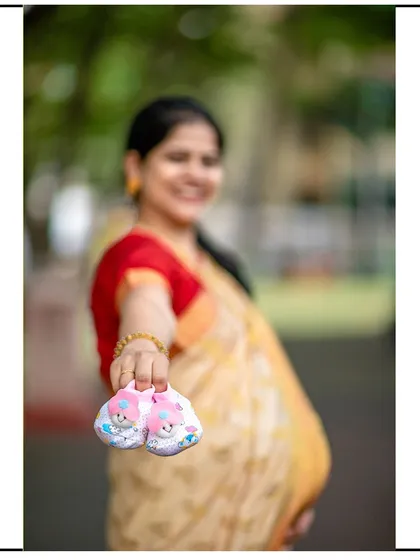 A creative shot with the focus on the baby shoes held out by the mom-to-be, who is smiling in the background.