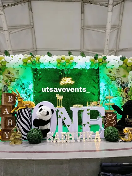 A wide view of the jungle-themed first birthday stage, showing the full arrangement of animal props, 'ONE' letters, and the green-lit backdrop.
