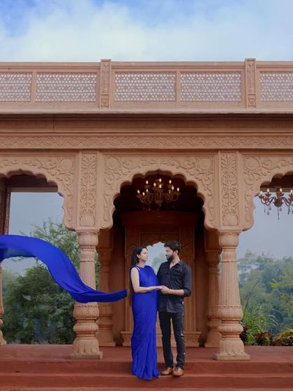 A breathtaking wide shot at a palace, with the blue of the flowing dress creating a stunning contrast against the warm stone architecture. This is a perfect example of a cinematic pre-wedding photo.