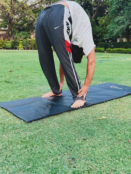 A standing forward bend, or Uttanasana, demonstrated in a park. This pose is great for calming the mind and stretching the hamstrings.