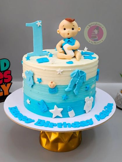 A sweet blue ombre cake for a baby boy's first birthday, decorated with a fondant baby topper and tiny baby-themed elements.