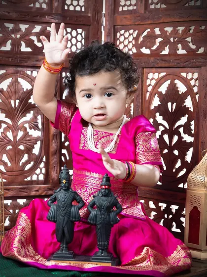 The same little girl raising her hand in a blessing pose, a playful and adorable moment from her traditional photoshoot.