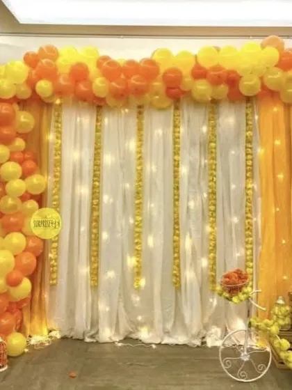 For pre-wedding functions, I design vibrant backdrops like this one for a Haldi ceremony. I use a combination of yellow and orange drapes and balloons, with fairy lights and marigold flower strings to match the traditional theme.