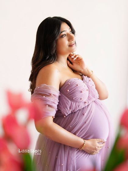 A thoughtful portrait of a mother-to-be looking towards the light. She is framed by pink tulips, wearing a lovely lavender gown, creating a soft and hopeful image.