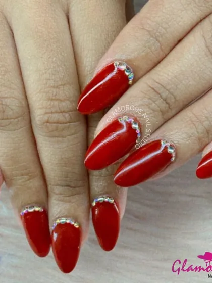 Classic red gets a glamorous upgrade. These bold, almond-shaped red nails are taken to the next level with a delicate arch of sparkling rhinestones at the cuticle, adding just the right amount of bling.