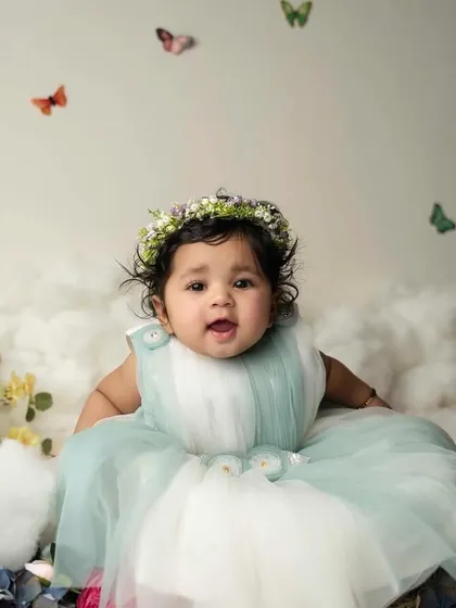A sweet, curious expression from this six-month-old baby girl. The whimsical butterfly and cloud backdrop adds a touch of magic to her milestone portrait.