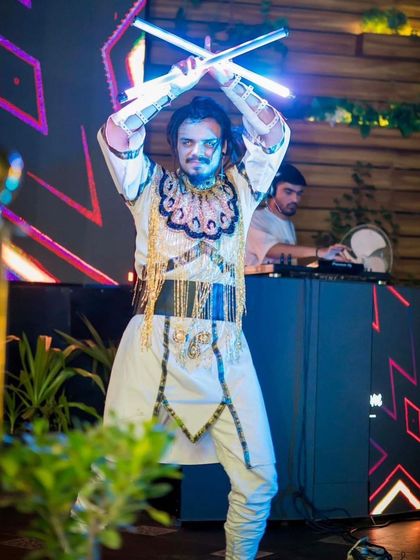 A male performer in an ornate white and gold costume wields two crossed LED staffs. This look is perfect for weddings or events with a royal or fantasy theme.
