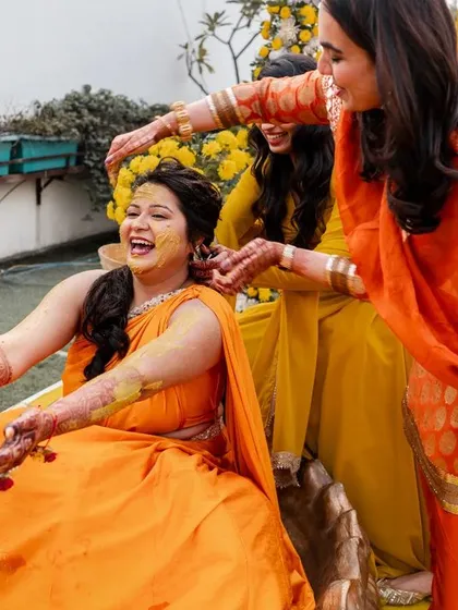 A candid moment of laughter and fun as the bride's friends apply Haldi during the pre-wedding ritual.