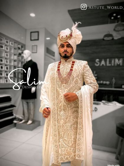 A groom in a classic off-white wedding sherwani. The piece is distinguished by its intricate, dense embroidery and is accessorized with a matching safa and a ruby necklace for a touch of color.