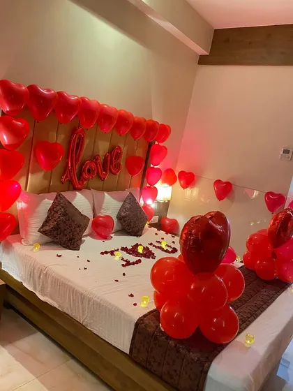 I can help you plan a special surprise with a romantic room decoration. This setup for an anniversary features a bed decorated with red heart-shaped balloons, a "Love" foil balloon, and balloon sculptures for a truly memorable celebration.