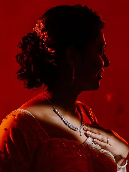 A silhouette of a bride against a bold red background, highlighting her profile and the details of her necklace.