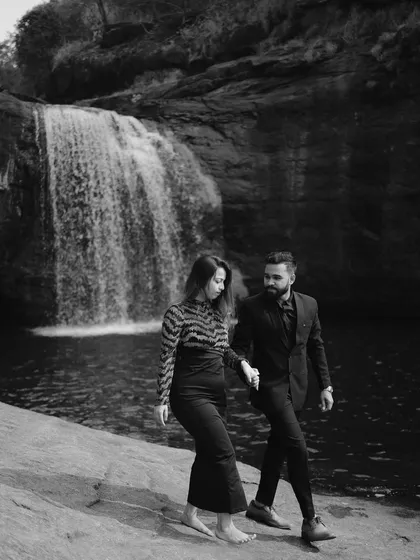 A dramatic black and white image of a couple walking by a waterfall, highlighting the contrast and texture of the natural landscape.