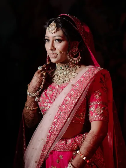 A dramatic and beautiful shot of the bride. The lighting highlights the glowing finish of the makeup and the rich colors of her pink lehenga, creating a truly cinematic feel.