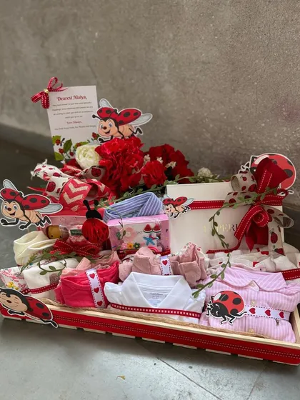 A full tray of "ladybug love" for a baby announcement. This hamper is packed with baby clothes and essentials, all meticulously arranged and decorated with a cheerful ladybug motif.