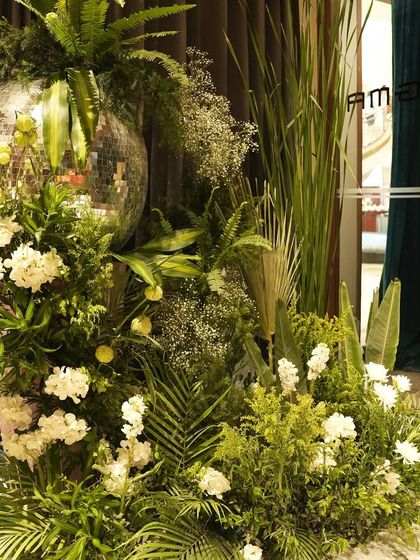 A detail shot of a floral arrangement from the jungle party, where a disco ball is nestled amongst white flowers and a variety of green leaves. This shows the creative and playful fusion of different design elements.