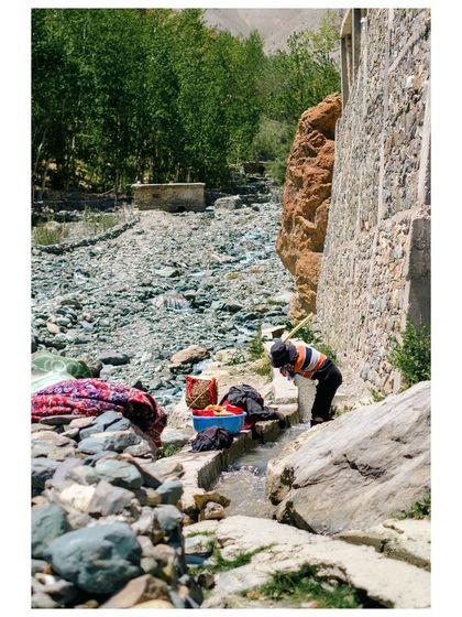 A person washes clothes in a small stream flowing through the rocky landscape of Zanskar.