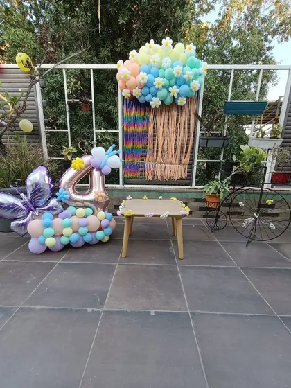 A full view of the outdoor setup for a butterfly and floral 4th birthday. The arrangement includes a custom backdrop, a number '4' balloon bouquet, and a small table for activities or cake, creating a complete party corner.