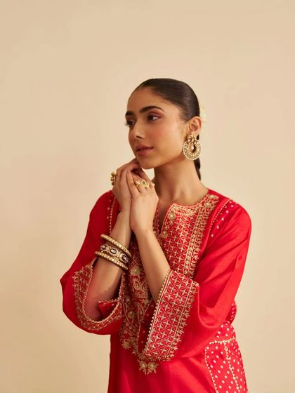 A close-up of a model in a vibrant red kurta, her look completed with traditional bangles, showcasing the rich color and detailed embroidery.