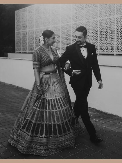 A classic black and white shot of the groom in a tuxedo walking with his bride in a lehenga. This image beautifully blends Western and Indian wedding styles with a timeless, old-world charm.
