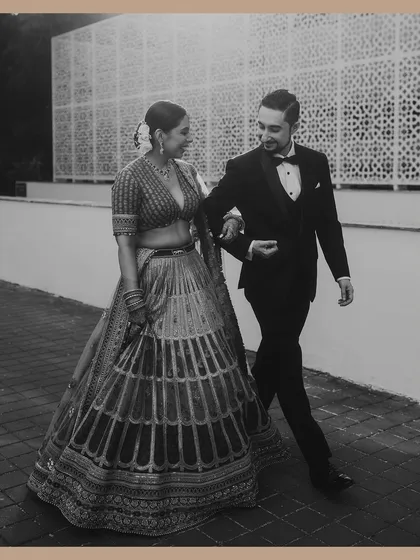 A classic black and white shot of the groom in a tuxedo walking with his bride in a lehenga. This image beautifully blends Western and Indian wedding styles with a timeless, old-world charm.