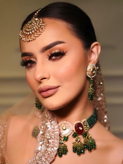 A glamorous look featuring a kundan and emerald choker with a ruby centrepiece, paired with a large maang tikka. Perfect for making a statement at any event.