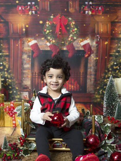 A big, happy smile from a toddler enjoying the Christmas sleigh setup, surrounded by presents and ornaments.