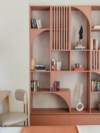 This custom bookshelf in a beautiful terracotta hue serves as both a storage unit and a sculptural element in the room. The design incorporates arches and slats, adding texture and a unique architectural feature to the study area.