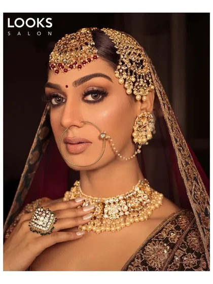 A powerful and direct bridal portrait. The focus here is on the eyes, which are enhanced with kohl and long lashes, and the intricate details of her passa and tikka. This is a classic, bold bridal statement.
