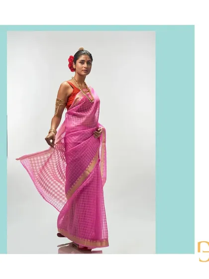 The light and playful nature of the mystic pink organza saree is captured in this dynamic pose, highlighting its checked pattern.