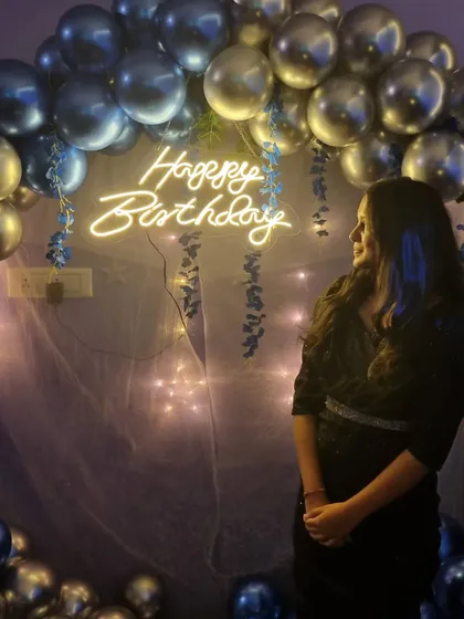 A guest enjoying the birthday setup. The combination of the neon sign, fairy lights, and metallic balloons creates a festive and highly photogenic environment.