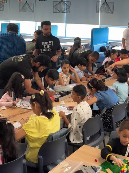 Our mentor, wearing a "Build the Future" shirt, guides a group of enthusiastic children at a building table during the large-scale MetLife corporate event.