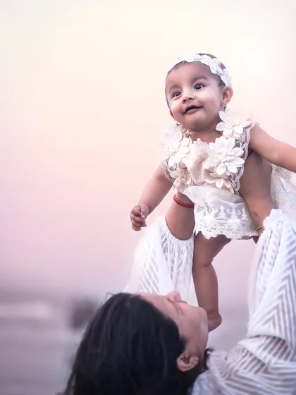 A mother lifts her baby girl high in the air at the beach. The baby's expression of delight and wonder is absolutely priceless.