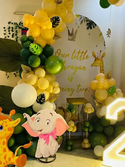 A "Wild Two" jungle-themed birthday party. This decoration features a custom backdrop, cute giraffe and elephant cutouts, a marquee number '2', and a green and yellow balloon garland.