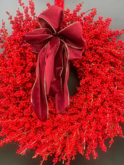 A wreath made entirely of vibrant red ilex berries. This striking, minimalist design makes a bold statement, with a luxurious velvet bow adding the final touch of elegance.