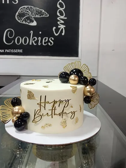 A chic white birthday cake with black and gold spheres, gold leaf, and elegant fan decorations.