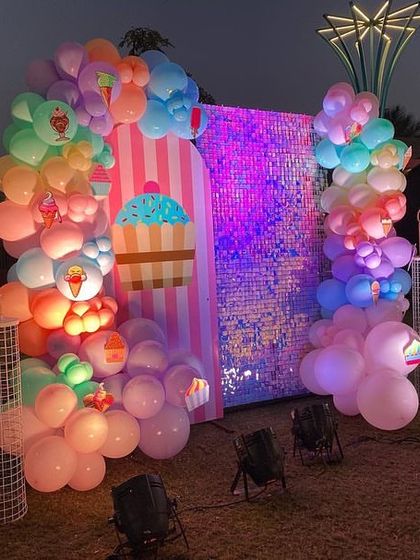 A fun photo booth area for the Candyland party, with a pink and white striped backdrop, a shimmering sequin wall, and colorful balloon garlands.